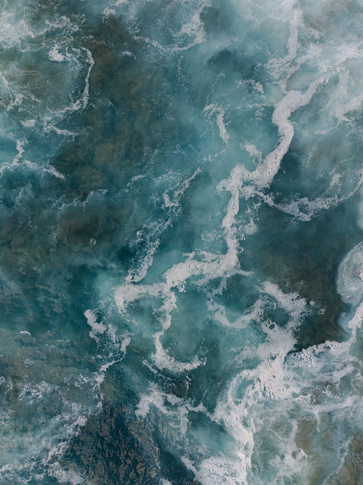 An aerial view of turquoise ocean water turning over itself, the constantly changing environment microalgae evolved in