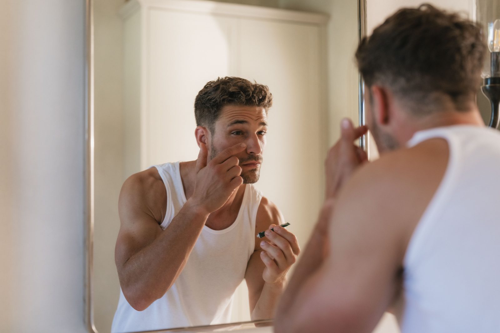 A man applying moisturiser at a bathroom mirror