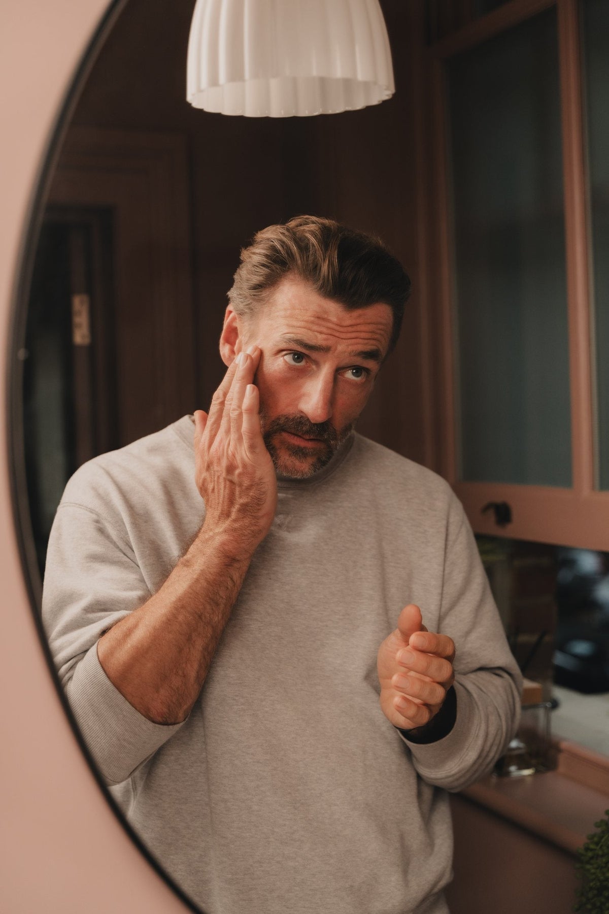 A man at a round mirror at home, applying eye serum