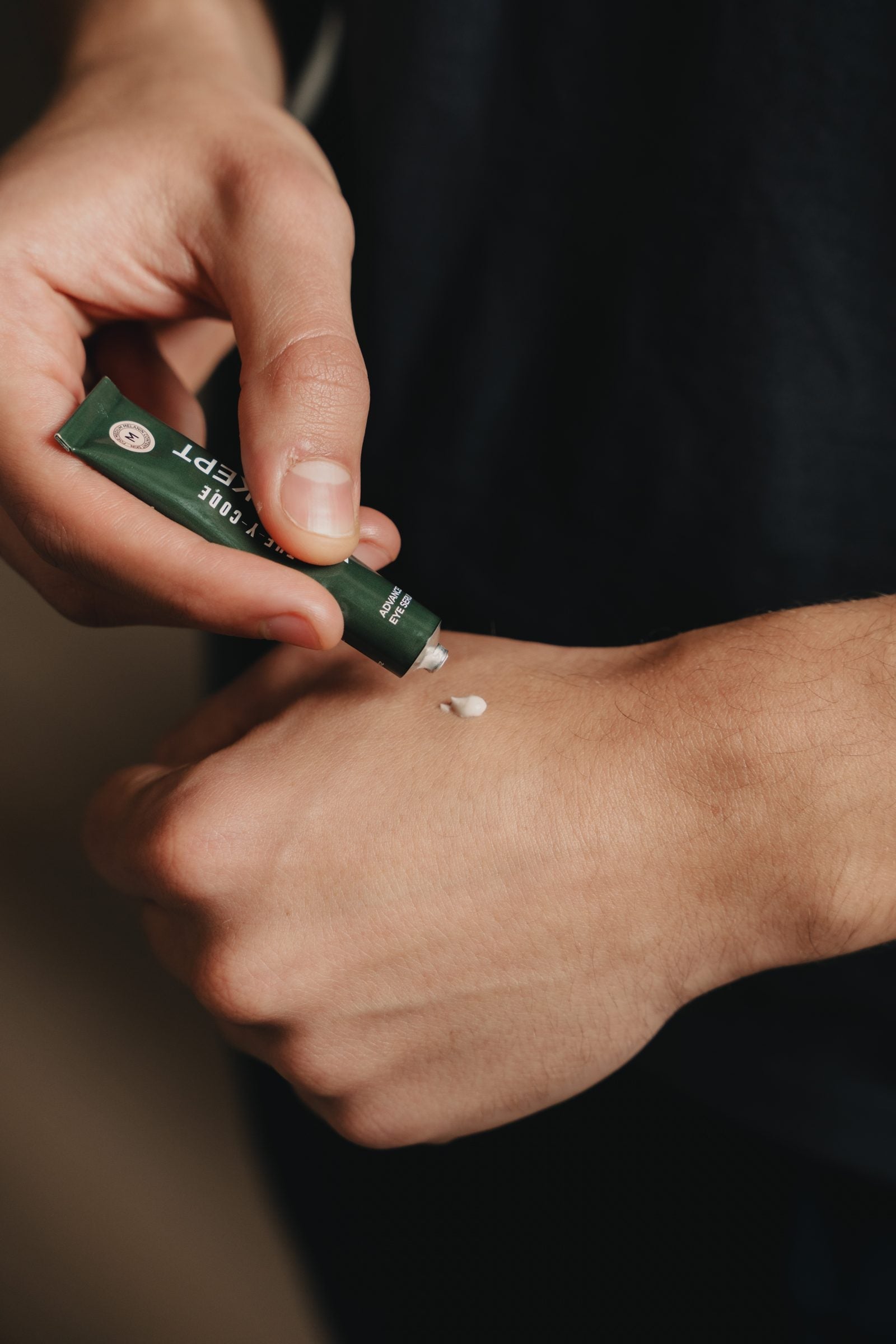 A man swatching the YCODE Advanced Eye Serum onto the back of his hand, showing the light serum texture