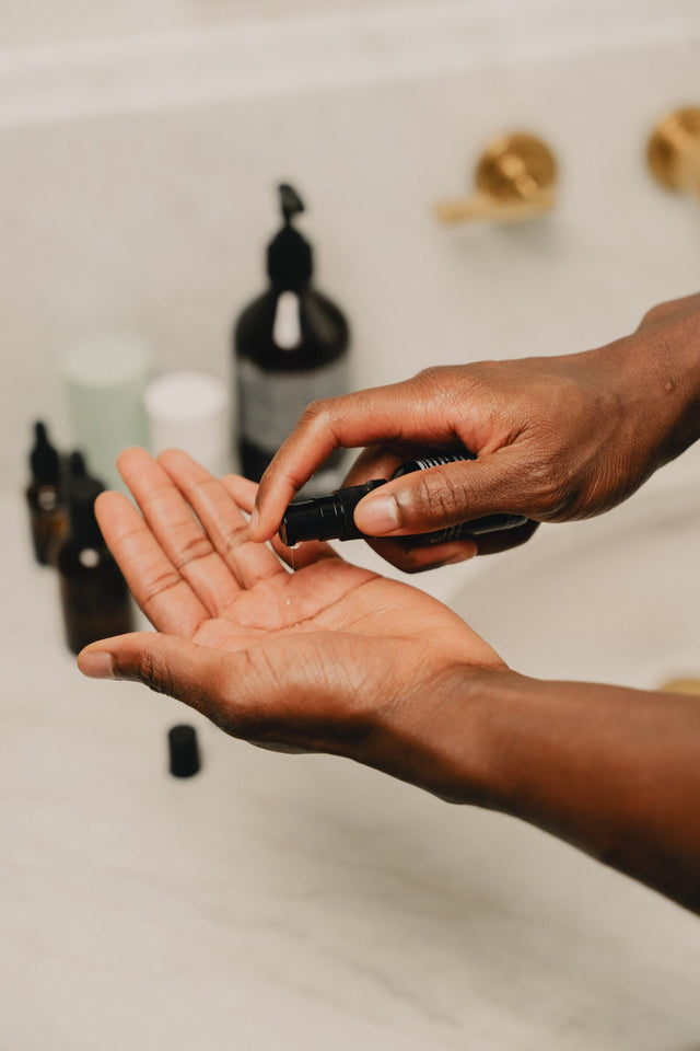 A serum drop dispensed into an open palm, with skincare bottles behind