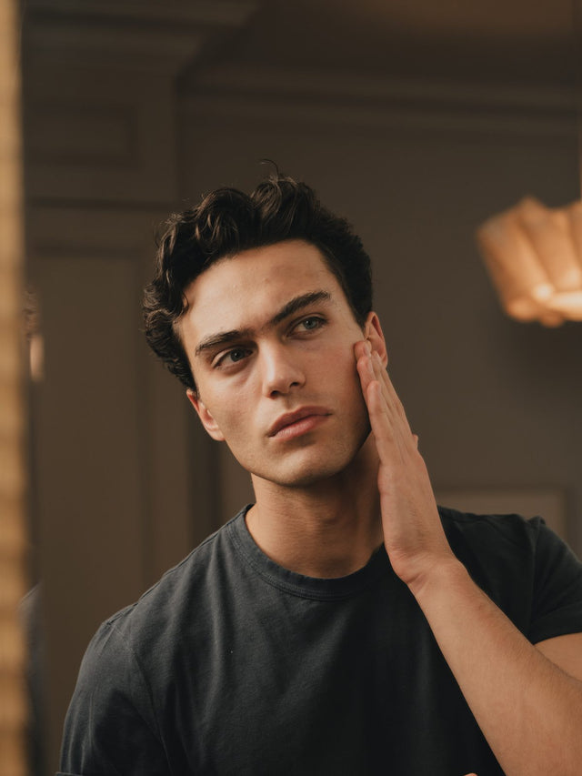 A man applying skincare at a mirror in warm autumn light