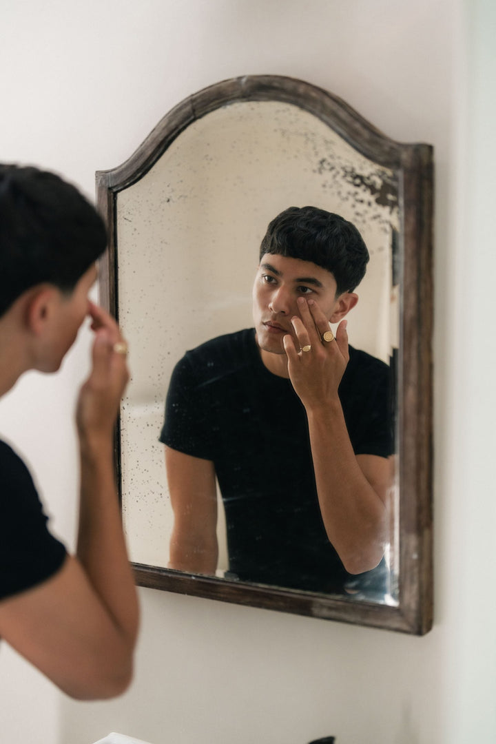 A man applying eye serum at a mirror