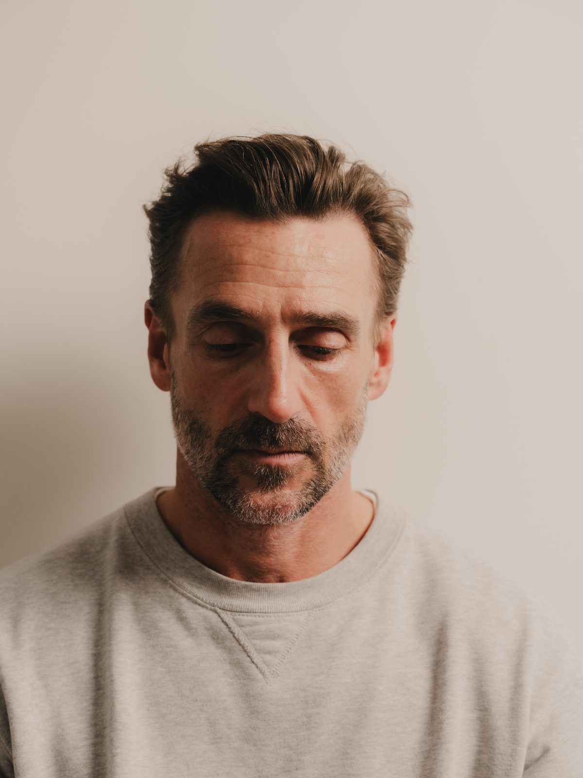 A man in his forties looking down, photographed in soft daylight